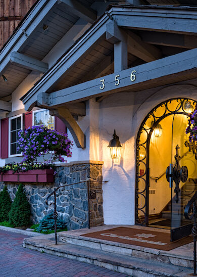 A quaint building with a stone and wood exterior features hanging flower baskets, an ornate entrance, and the number 356 above the door.