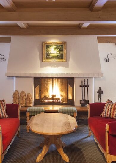 A cozy living room with two red sofas, a wooden coffee table, and a fireplace flanked by windows. Decor includes a painting above the fireplace.