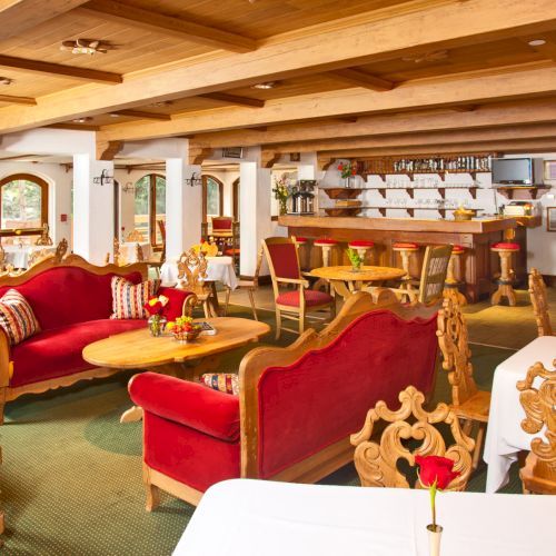 A cozy restaurant with wooden furniture, red upholstered seating, white tablecloths, and decorative plates on the wall, creating a warm atmosphere.